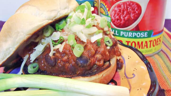 A closeup horizontal image of a Sloppy Jose Pork Sausage Sandwich with black beans and scallions.