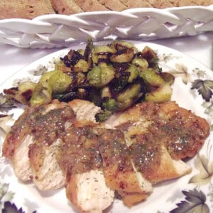 A sliced serving of Chicken with Mustard Dill Sauce on a plate with brussels sprouts.