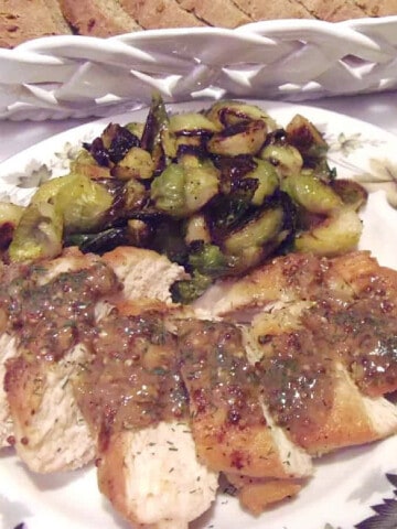 A sliced serving of Chicken with Mustard Dill Sauce on a plate with brussels sprouts.