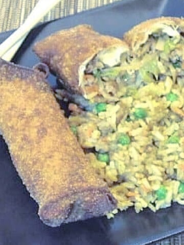 Two Homemade Egg Rolls on a square black plate with chopsticks and fried rice.