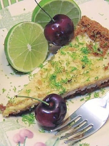 A serving of Key Lime Tart on a plate with a fork, lime slices and cherries.