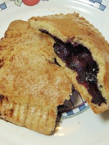 A broken in half Browned Butter Blueberry Hand Pie on an old-fashioned plate.