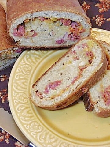 Two slices of a Reuben Sandwich Roll on a yellow plate with a napkin underneath.