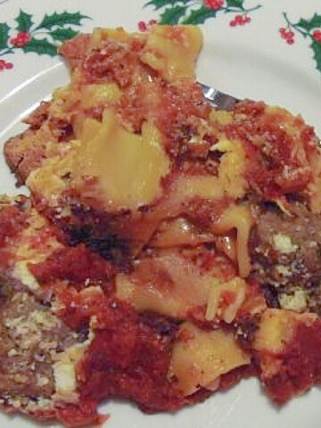 A messy serving of Crockpot Lasagna on a holly berry plate.