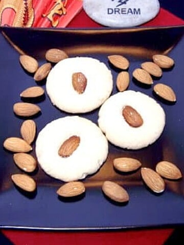 Three Chinese Almond Cookies on a square black plate with almonds.