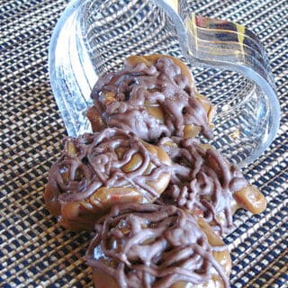 Homemade Pecan Turtle Candy spilling out of a glass heart candy dish.