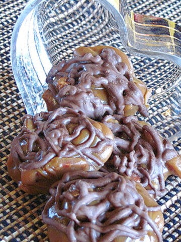 Homemade Pecan Turtle Candy spilling out of a glass heart candy dish.