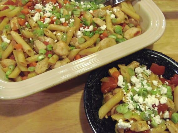 A rectangle casserole dish and black bowl filled with Buffalo Chicken Pasta topped with blue cheese.