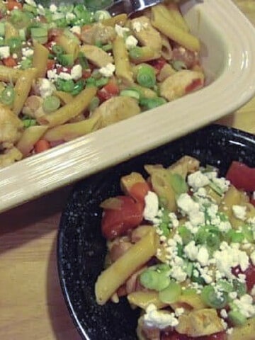 A rectangle casserole dish and black bowl filled with Buffalo Chicken Pasta topped with blue cheese.