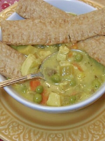 A small bowl of Chicken Pot Pie Soup with pie crust dippers on top.