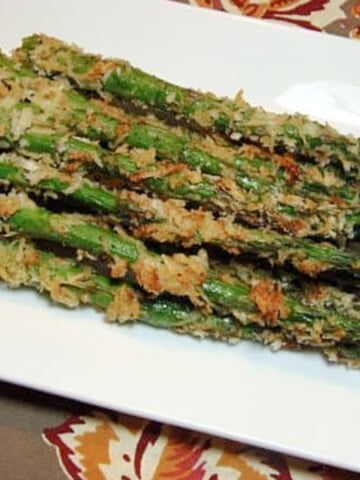 A rectangle white platter filled with Parmesan Crusted Asparagus spears.
