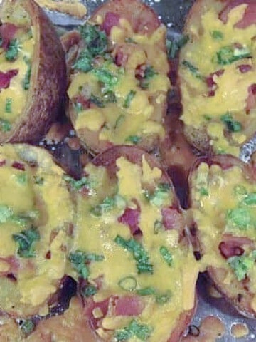Some Loaded Homemade Potato Skins on a baking sheet with melted cheese, scallions, and bacon.