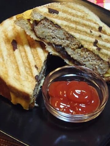 A Turkey Patty Melt that's been cut in half with a small dish of ketchup on a black plate.