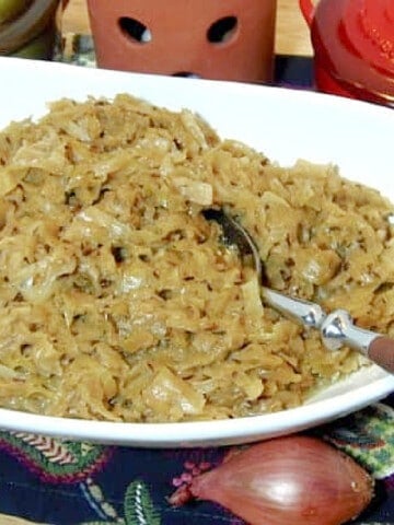 A white oval bowl filled with Creamy Cabbage with Caraway and Thyme and a serving spoon.