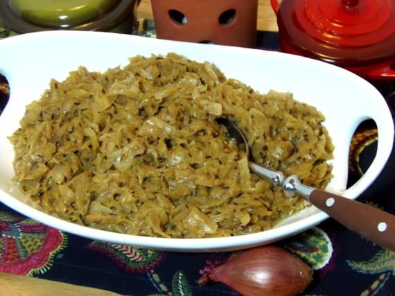 A white oval bowl filled with Creamy Cabbage with Caraway and Thyme and a serving spoon.