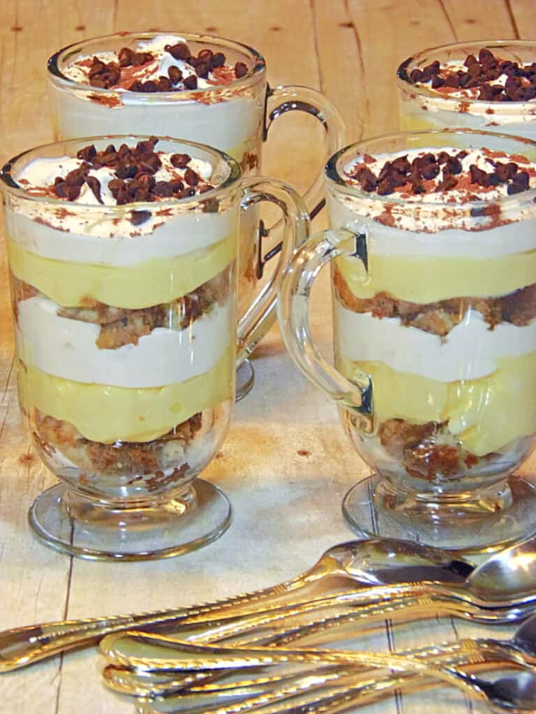 A vertical photo of four Irish coffee mugs filled with layered Skinny Tiramisu Parfaits with chocolate chips and whipped cream.