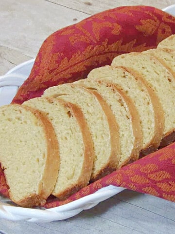 A ceramic white basket filled with slices of Cornmeal Yeast Bread and an orange napkin