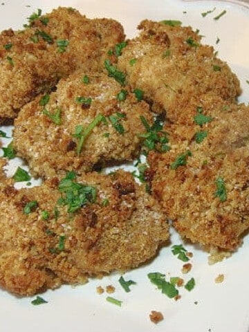 A white plate filled with Oven Fried Chicken Thighs and a parsley garnish.