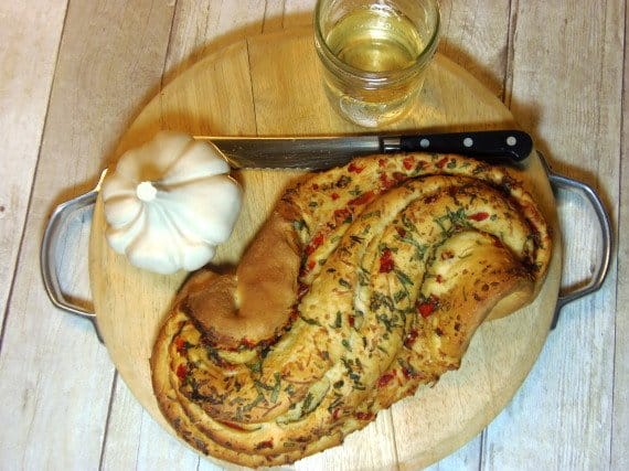 An overhead photo of a loaf of Paine Bianco with Red Peppers on a cutting board with a serrated knife and a glass of wine.