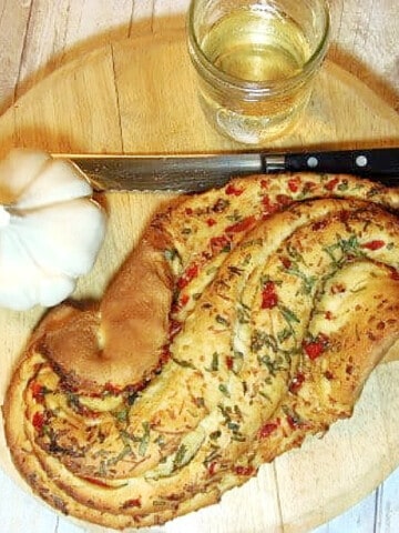 An overhead photo of a loaf of Paine Bianco with Red Peppers on a cutting board with a serrated knife and a glass of wine.