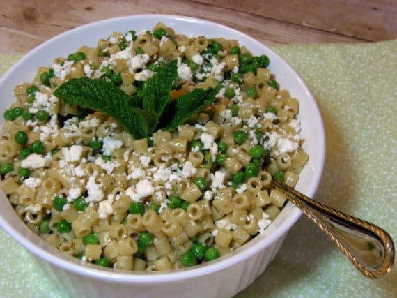 A round white bowl filled with chilled Greek Pasta Salad with Feta and Mint along with green peas.