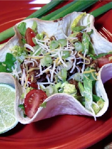 A Lighter Taco Salad is in a tortilla bowl and on a red plate with a lime and scallions.