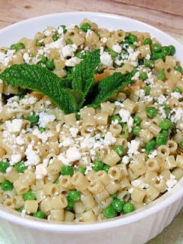A round white bowl filled with chilled Greek Pasta Salad with Feta and Mint along with green peas.