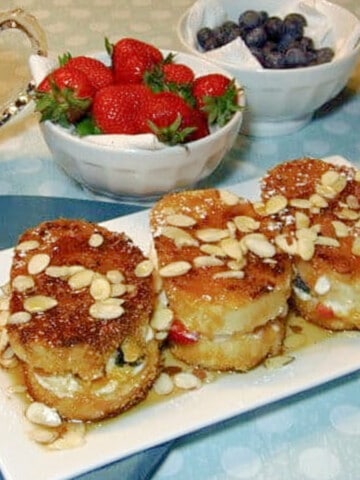 Three serving of Stuffed Red, White, and Blue French Toast on a white plate with slivered almonds on top.