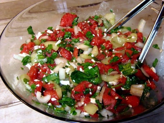 A glass bowl filled with Watermelon Cucumber Salad along with serving tongs.