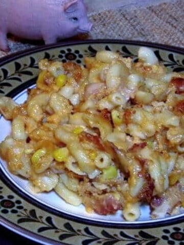 A plate of Bacon and Corn Macaroni and Cheese with a little pink piggy in the background.