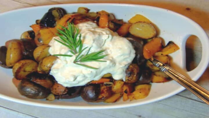 A white oval bowl filled with colorful new potatoes and a large dollop of sour cream and rosemary on top