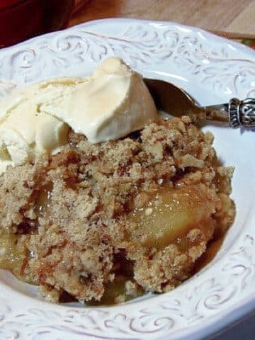 Some Adam's Apple Crisp in a white bowl with a scoop of melting vanilla ice cream.