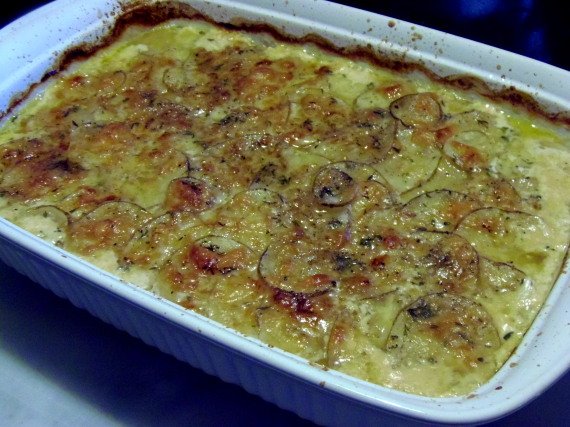 A white rectangle baking dish filled with brown and cheese Potato Gratin with Beer Cheese Sauce.