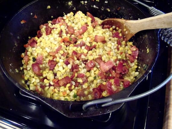 Closeup photo of fried corn with bacon in a cast iron pan.