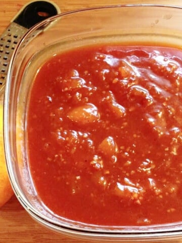 A glass bowl filled with Peach BBQ Sauce with an orange on the side.