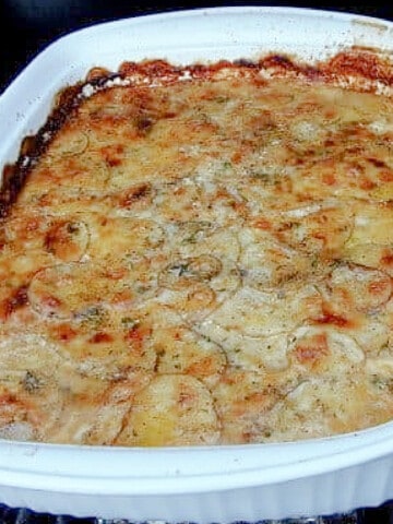 A white rectangle baking dish filled with brown and cheese Potato Gratin with Beer Cheese Sauce.