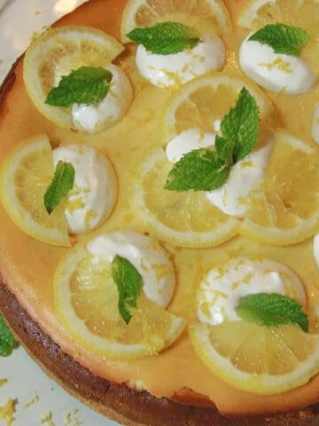 A Lemon Cheesecake with dollops of cream, mint, and lemon slices.