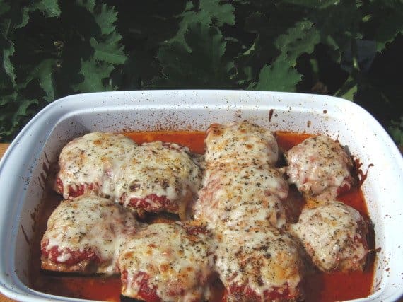 A white casserole dish filled with Turkey Stuffed Zucchini Parmesan with melted cheese and Italian seasonings.