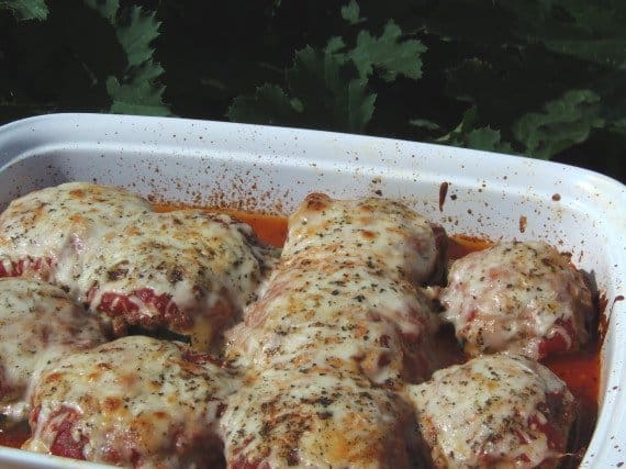 A white casserole dish filled with Turkey Stuffed Zucchini Parmesan with melted cheese and Italian seasonings.