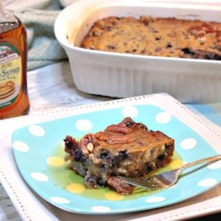 A square of blueberry sausage breakfast casserole on a plate with a bottle of maple syrup in the background.
