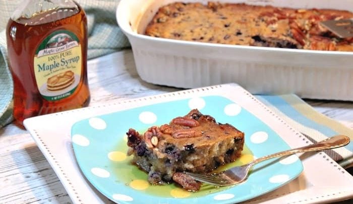 A square of blueberry sausage breakfast casserole on a plate with a bottle of maple syrup in the background.