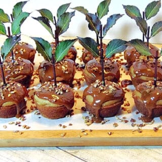 A wooden tray filled with Caramel Apple Cupcakes along with a stems, leaves, and chopped pecans.