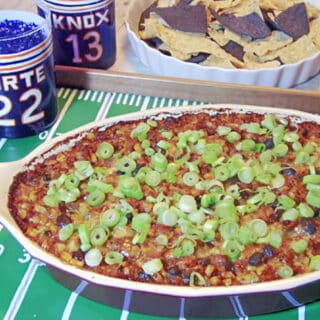 A baking dish filled with Cheesy Corn and Black Bean Dip on a painted football field tray.