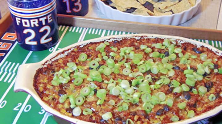 A baking dish filled with Cheesy Corn and Black Bean Dip on a painted football field tray.