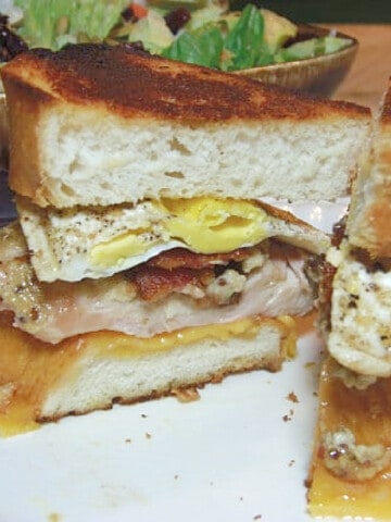 A Chicken and Egg Sandwich on a white plate with melted cheese and bacon.