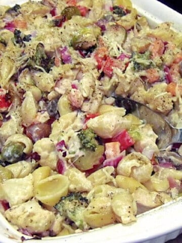 A white casserole dish filled with Chicken Pasta Casserole with Roasted Veggies and a serving spoon.