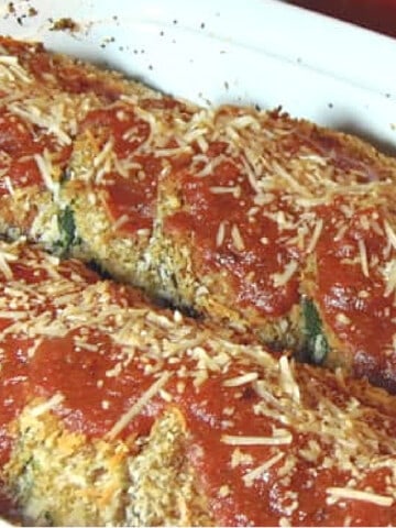 Slices of vegetables in a white casserole dish for Eggplant and Zucchini Parmesan covered with tomato sauce and cheese.