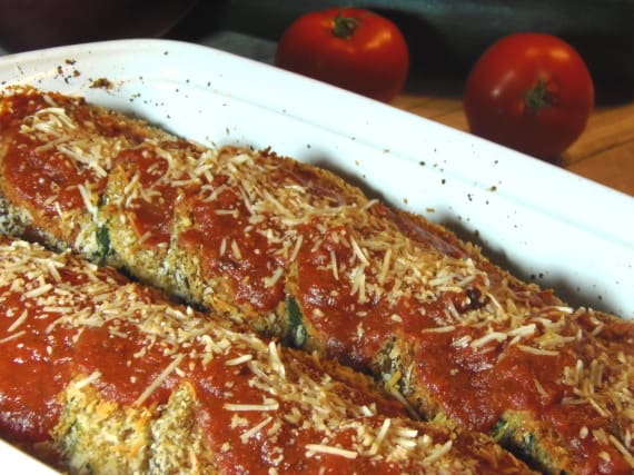 Slices of vegetables in a white casserole dish for Eggplant and Zucchini Parmesan covered with tomato sauce and cheese.