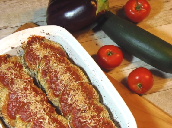 Slices of vegetables in a white casserole dish for Eggplant and Zucchini Parmesan covered with tomato sauce and cheese.