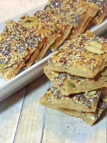 A stack of Savory Seed Crackers in the foreground and a line of crackers in the background.